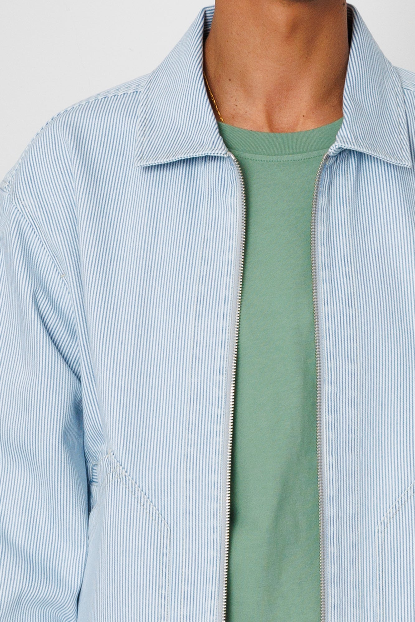 Light blue striped shirt over a green t-shirt on a neutral background