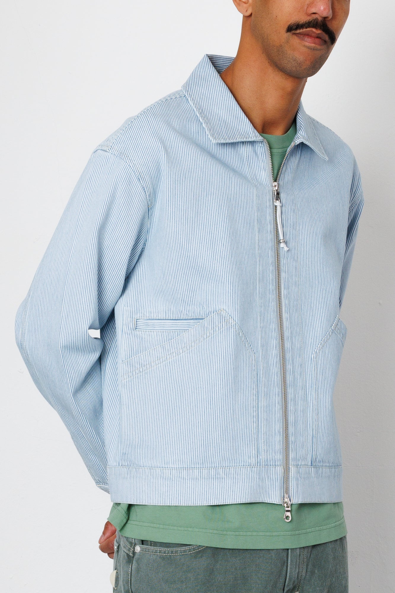 Man wearing a light blue corduroy jacket with a zipper on a plain background