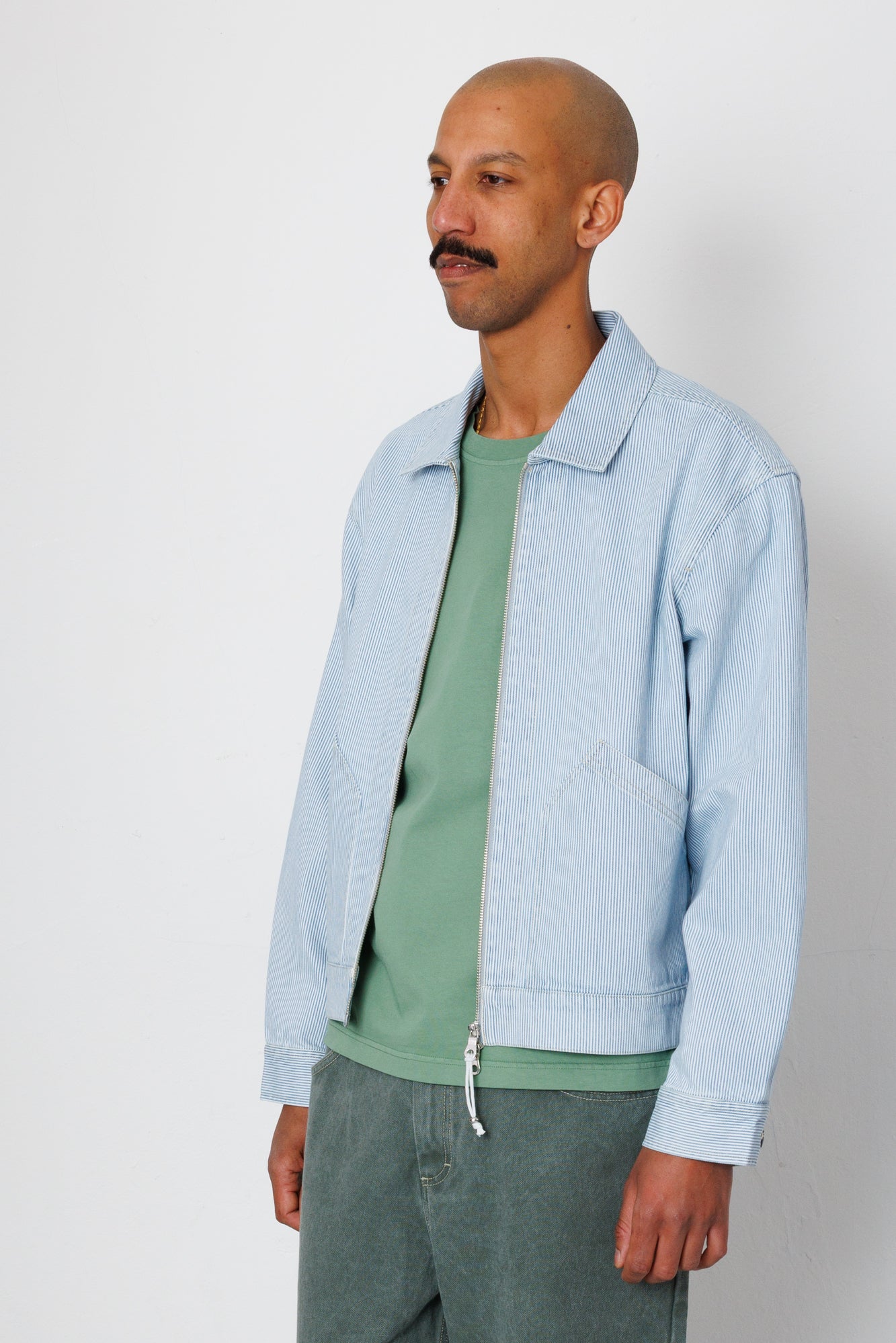 Man wearing a light blue jacket over a green shirt on a white background