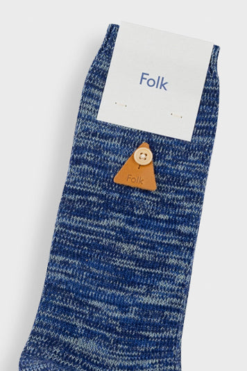 A single blue marled knit sock with a small brown leather triangle button featuring a wooden button, with a white paper header card that says 'Folk'.