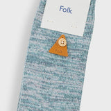 A single light blue and white heathered knit sock with a small orange-brown leather button featuring a cartoon face, shown with a white paper tag printed with the brand name 'Folk'.