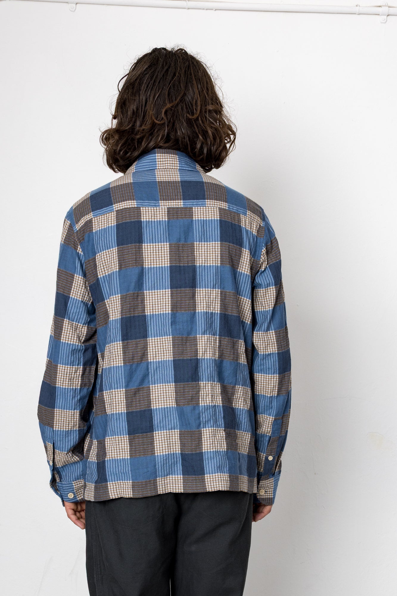 Person wearing a blue and brown plaid shirt against a white background