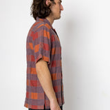 Man wearing a plaid shirt standing against a white wall