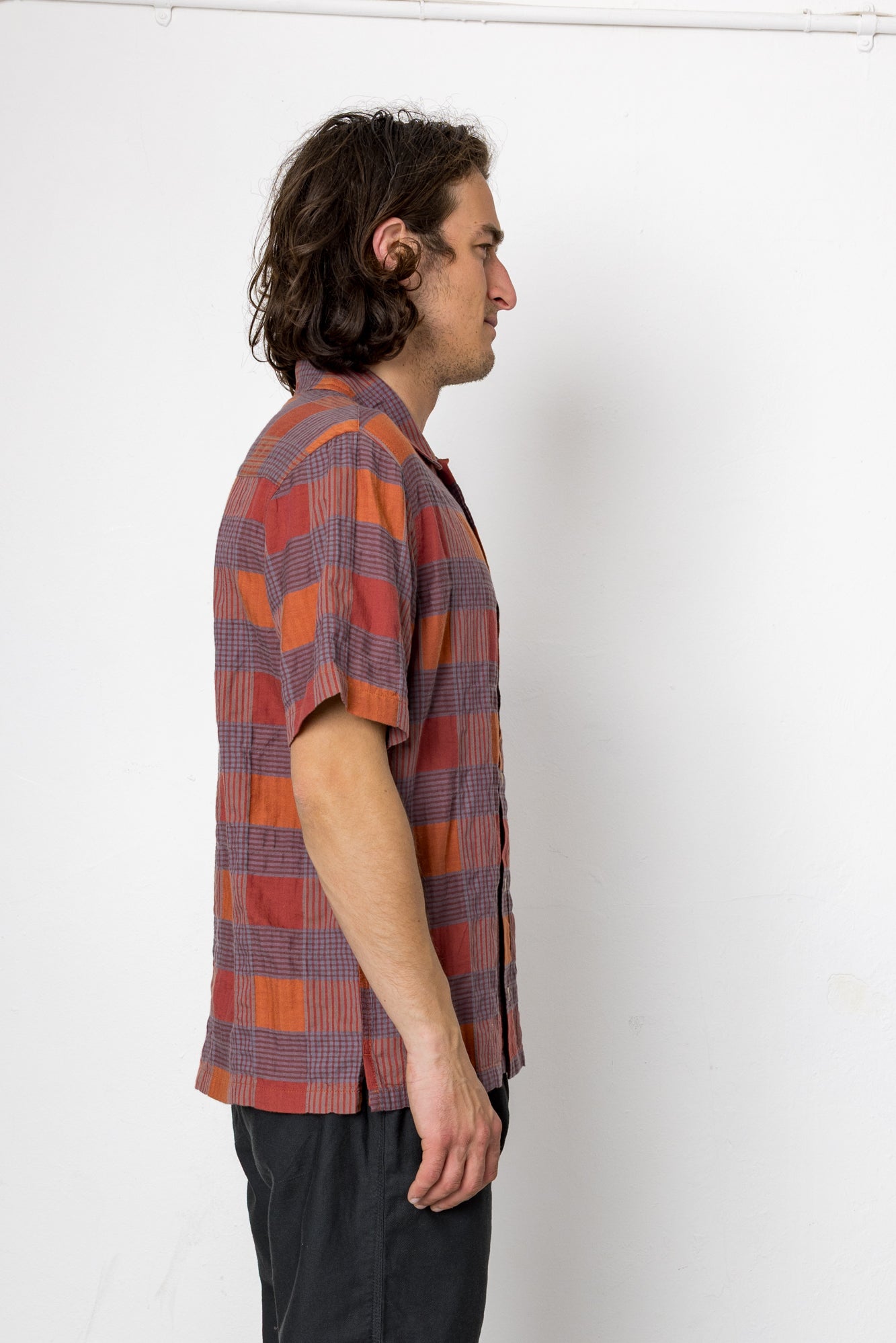 Man wearing a plaid shirt standing against a white wall