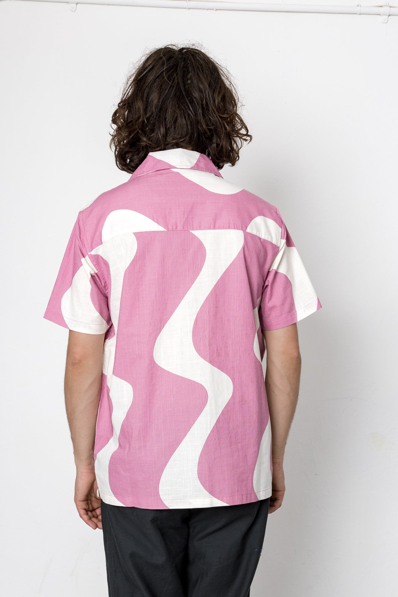 Person wearing a pink and white patterned shirt on a plain background