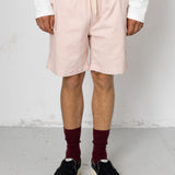 Person wearing light pink shorts, maroon socks, and black shoes on a plain background