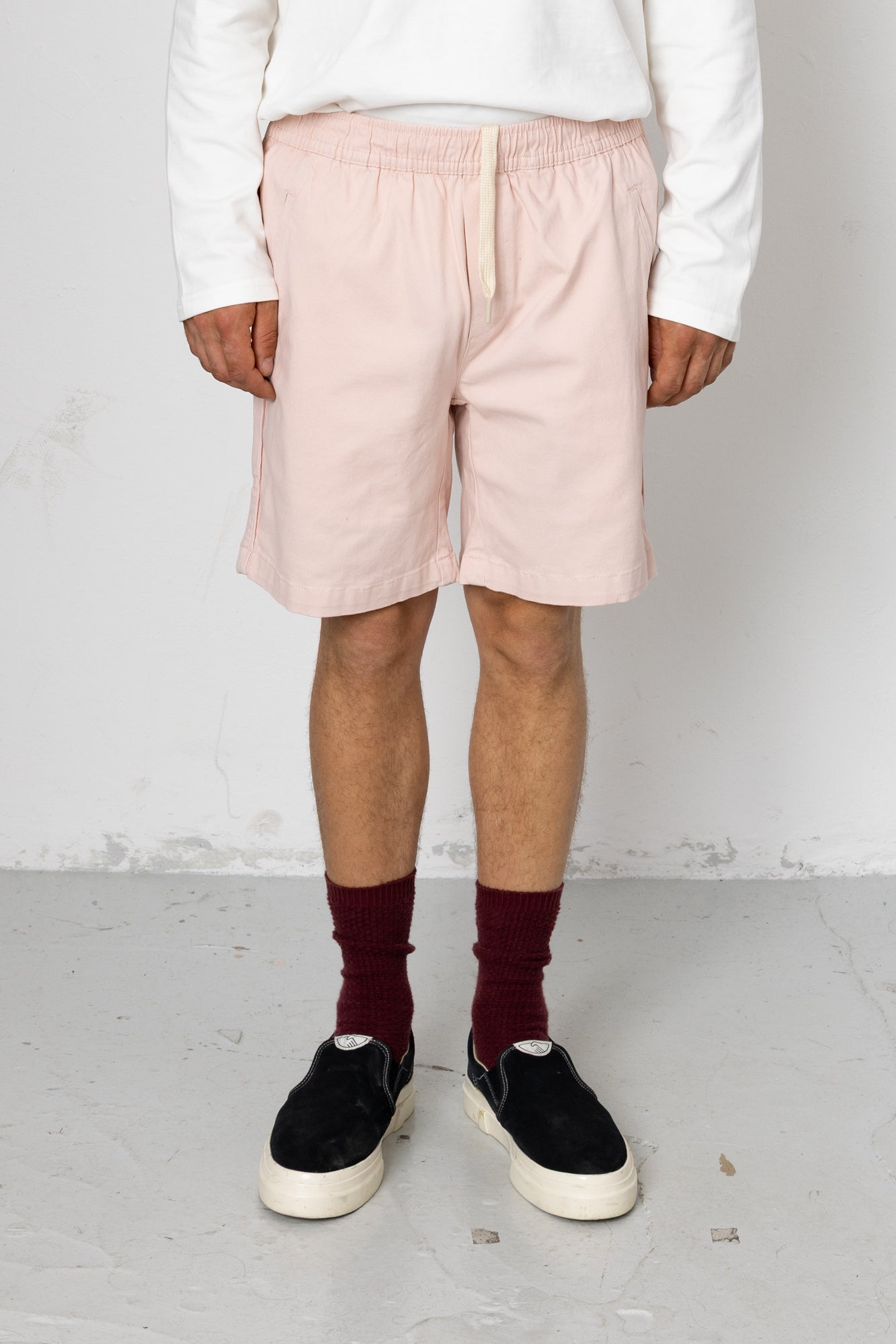 Person wearing light pink shorts, maroon socks, and black shoes on a plain background