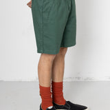 Person wearing green shorts, white shirt, black shoes, and red socks on a white background