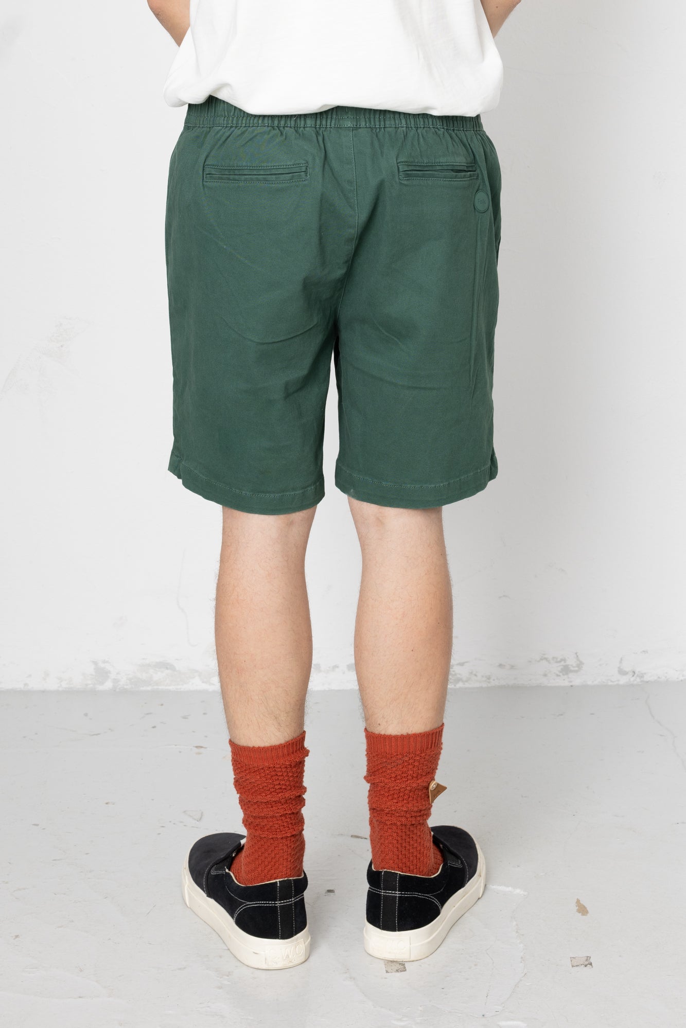 Person wearing green shorts and red socks with black shoes on a white background