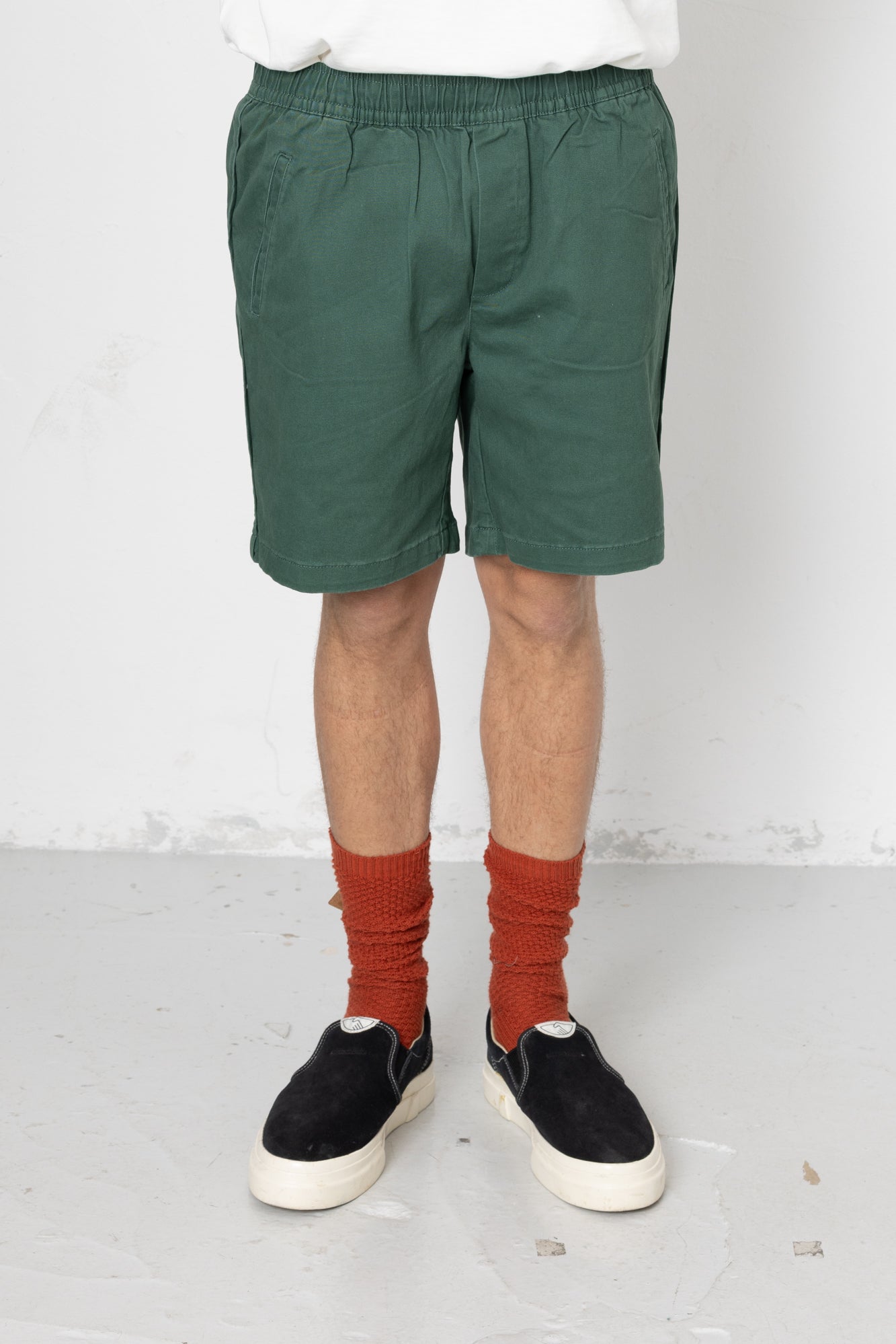 Person wearing green shorts, red socks, and black shoes on a white background