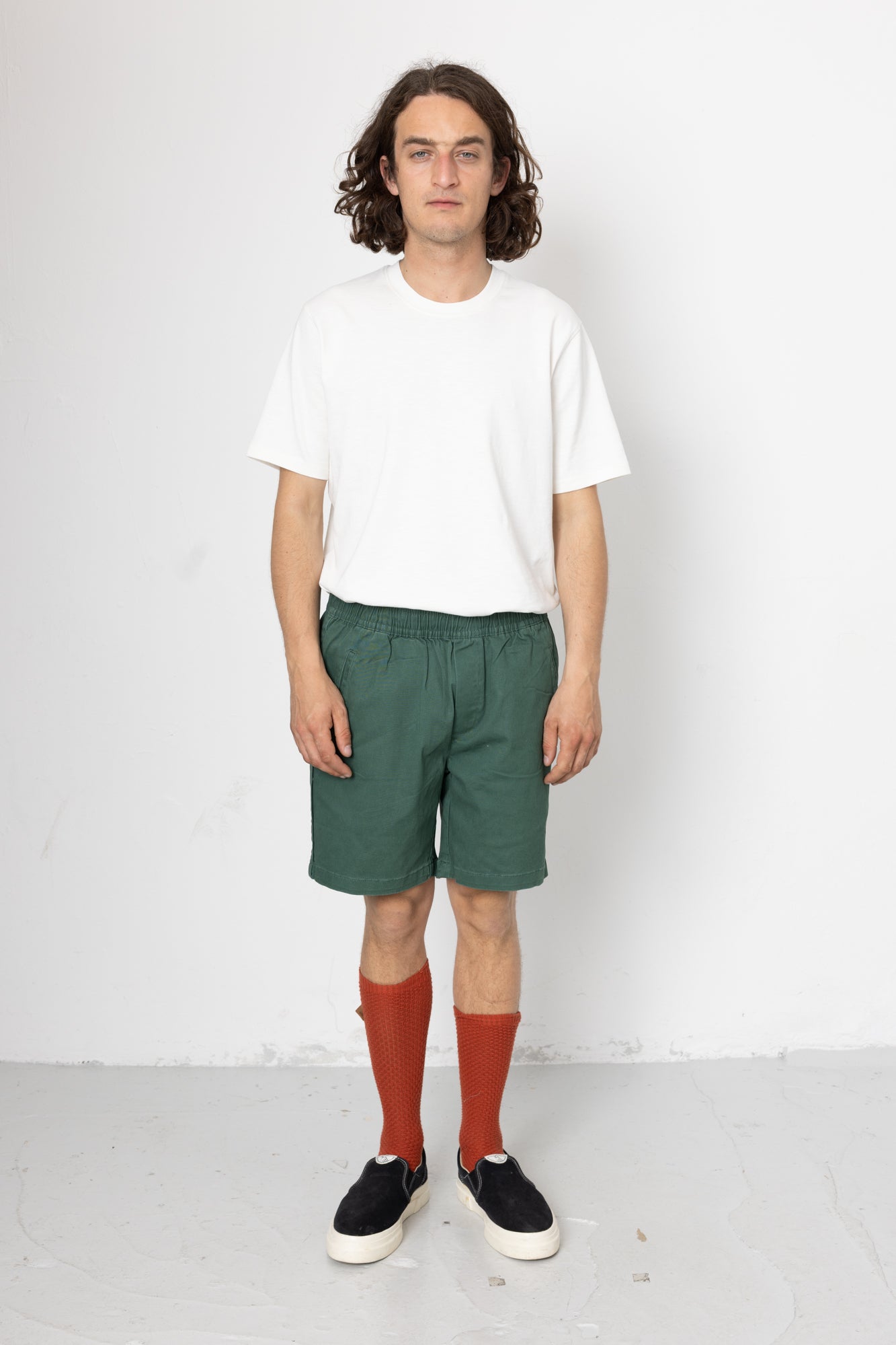 Person wearing a white t-shirt, green shorts, and red socks on a white background
