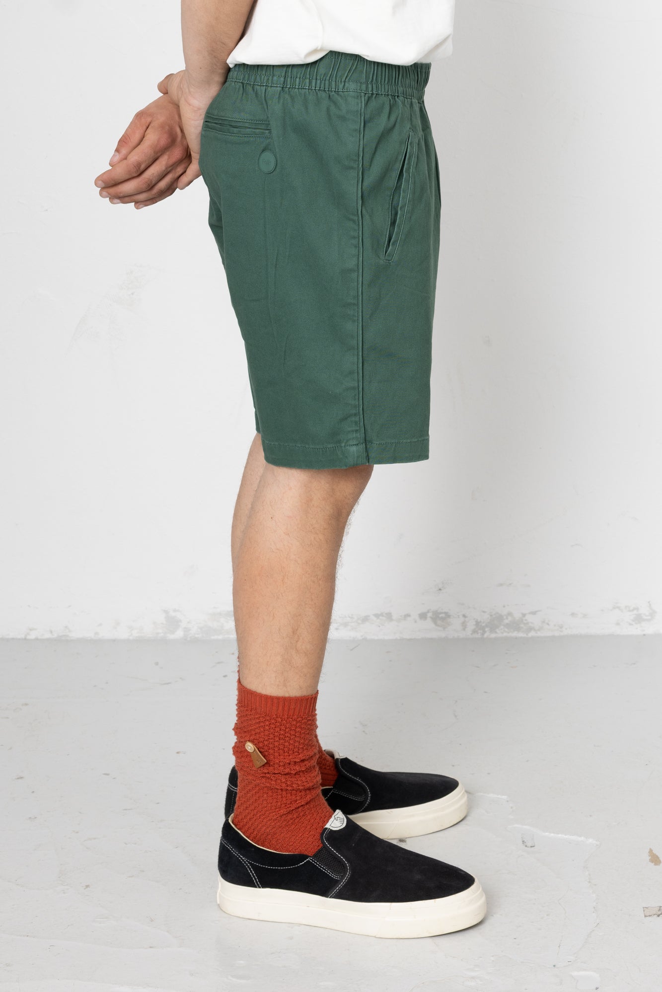 Person wearing green shorts, black shoes, and orange socks on a white background