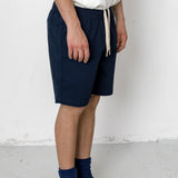 Person wearing navy shorts, white shirt, black shoes, and blue socks against a white background