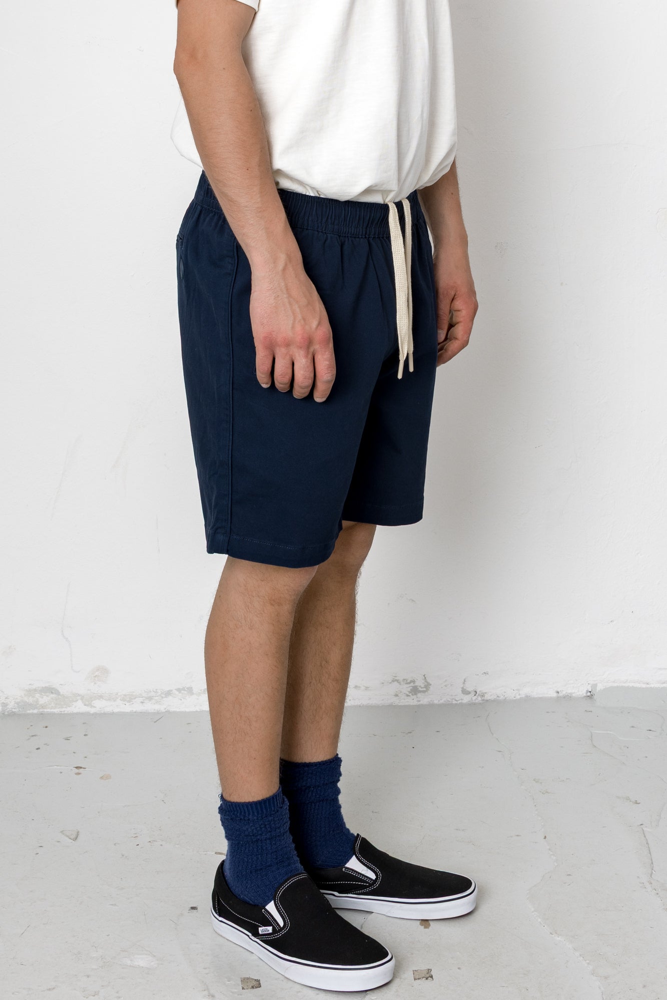 Person wearing navy shorts, white shirt, black shoes, and blue socks against a white background