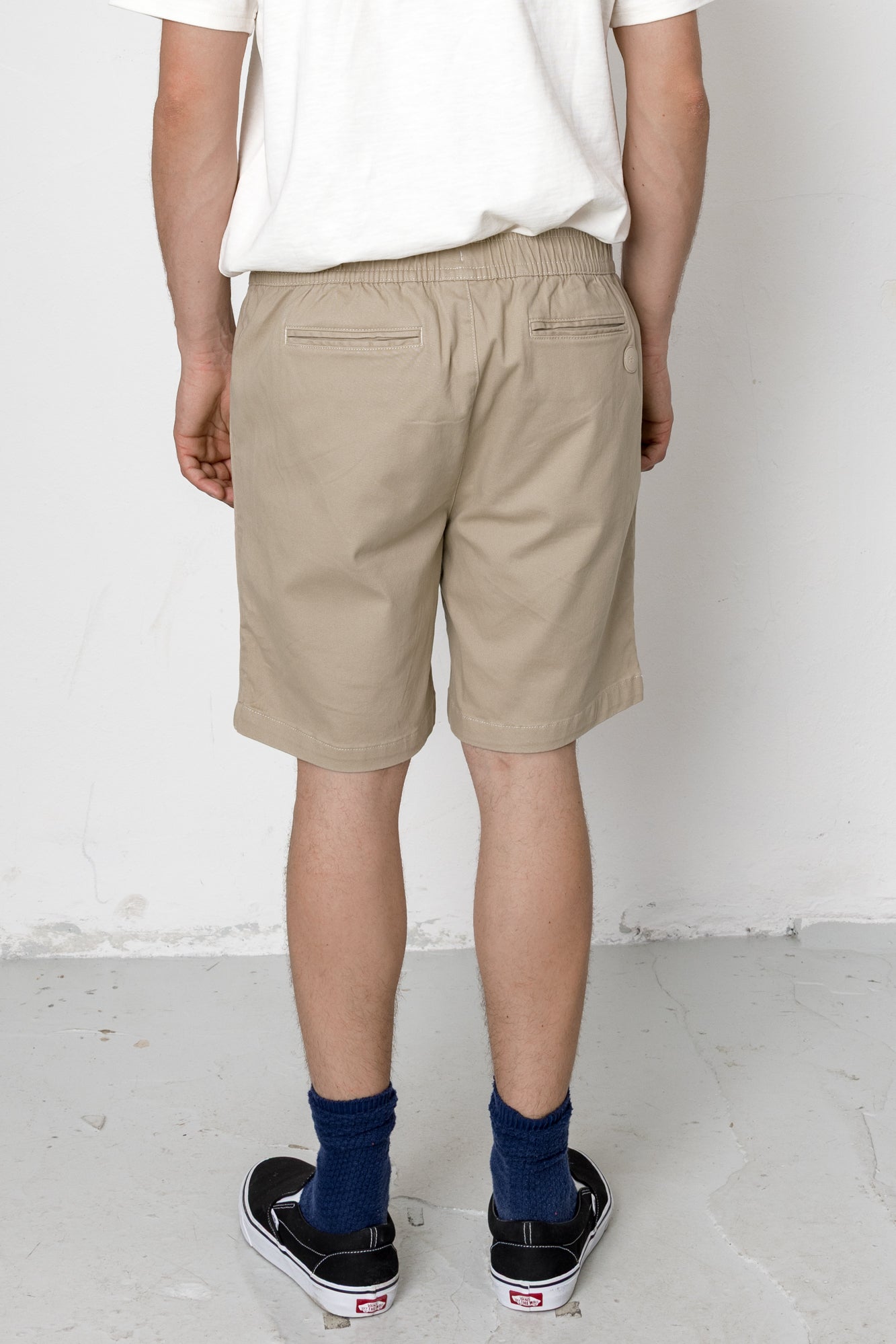 Person wearing beige shorts and navy socks with black shoes on a white background