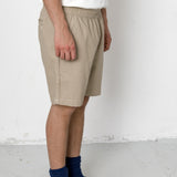 Person wearing beige shorts, white shirt, black shoes, and blue socks on a plain background