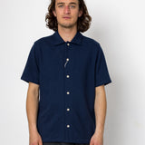 Man wearing a navy blue short-sleeve shirt with white buttons against a white background