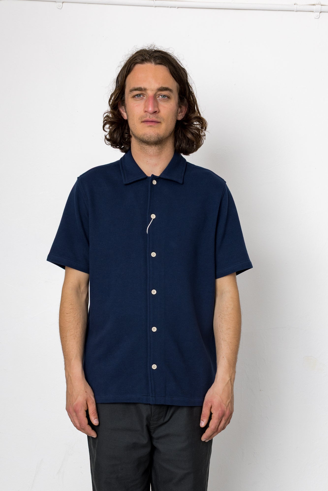 Man wearing a navy blue short-sleeve shirt with white buttons against a white background
