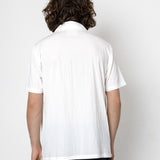 Person wearing a white polo shirt and dark pants against a plain background