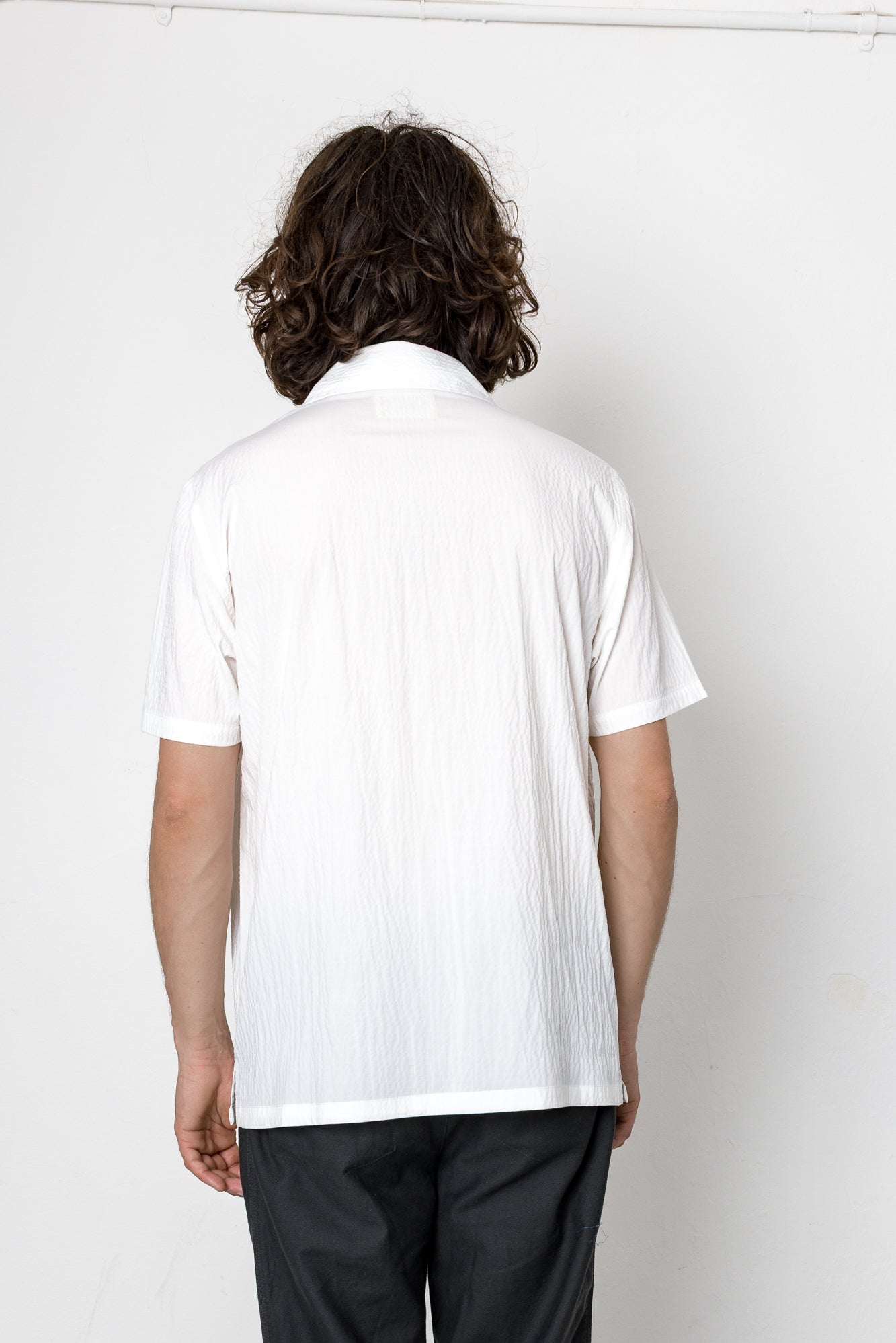 Person wearing a white polo shirt and dark pants against a plain background