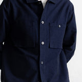 A man wearing a dark navy blue long-sleeve button-up overshirt over a white t-shirt, shown from the neck down against a white wall.