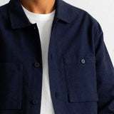 A close-up of a person wearing a dark navy blue button-up overshirt over a white t-shirt, against a plain white wall.