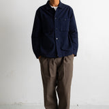 A man wearing a dark navy blue button-up overshirt, brown wide-leg trousers, and black-and-white sneakers, standing against a plain white studio wall.