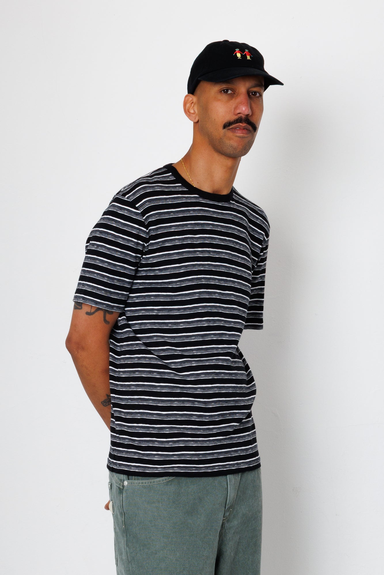 Man wearing a black and gray striped t-shirt and a black cap with a logo on a white background