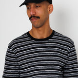 Man wearing a black and white striped t-shirt and a black cap with a small logo on a plain background