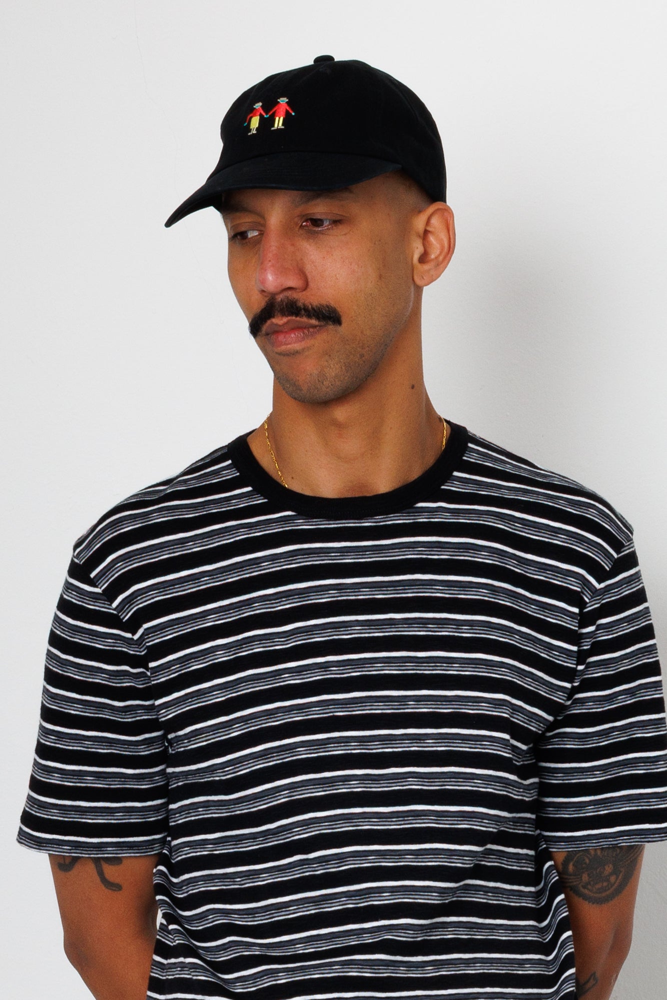 Man wearing a black and white striped t-shirt and a black cap with a small logo on a plain background