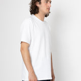 Man wearing a plain white t-shirt and dark pants on a light gray background