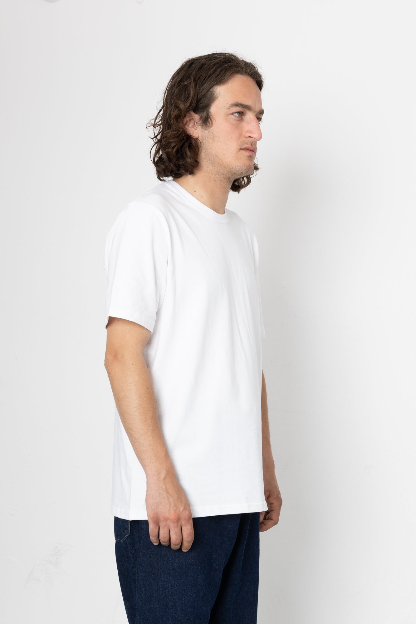 Man wearing a plain white t-shirt and dark pants on a light gray background