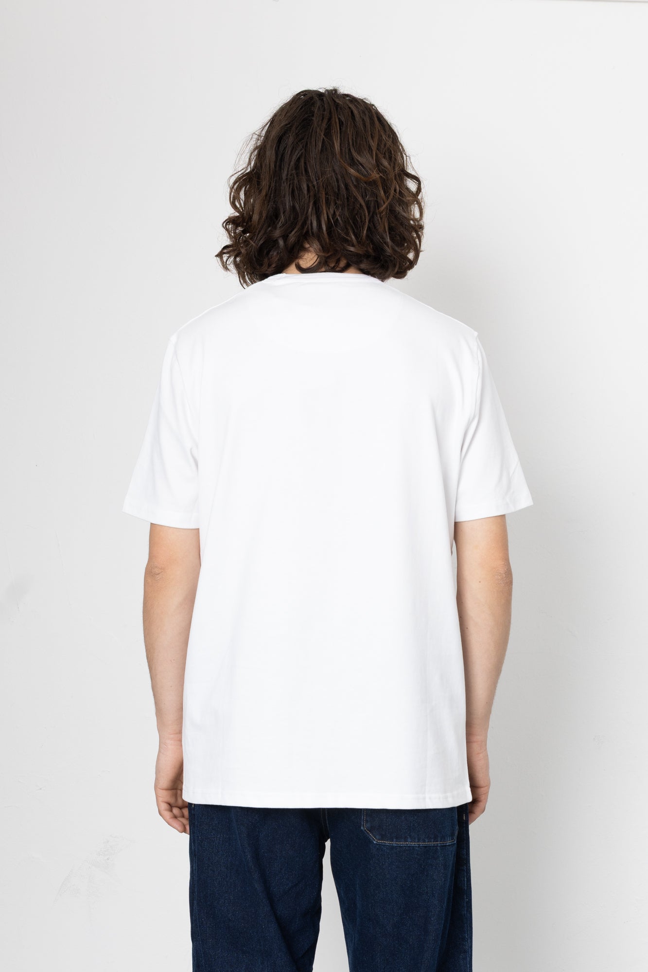 Person wearing a plain white t-shirt and dark jeans on a light gray background