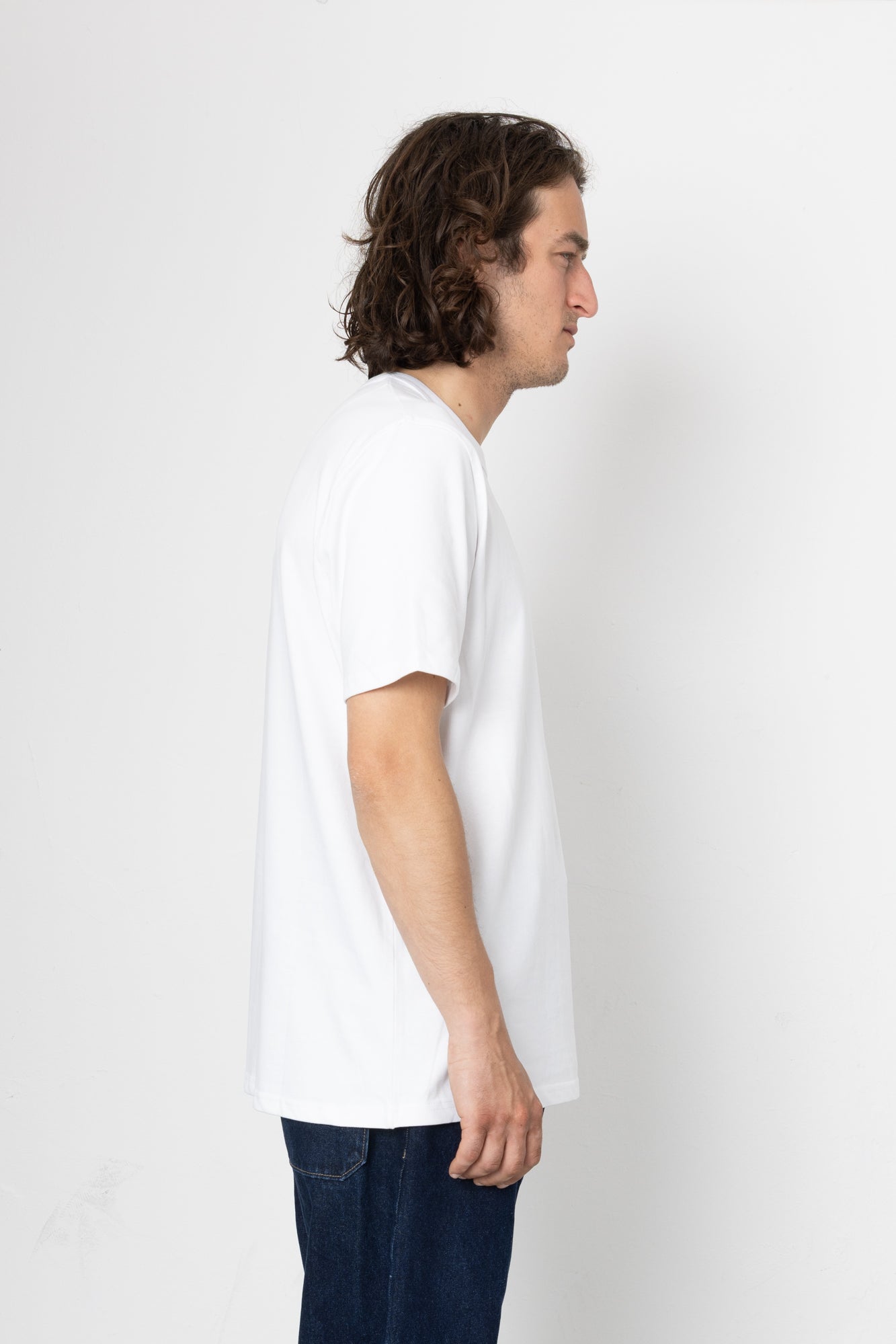 Man wearing a plain white t-shirt and dark jeans against a white background