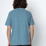 Person wearing light blue t-shirt facing a white wall