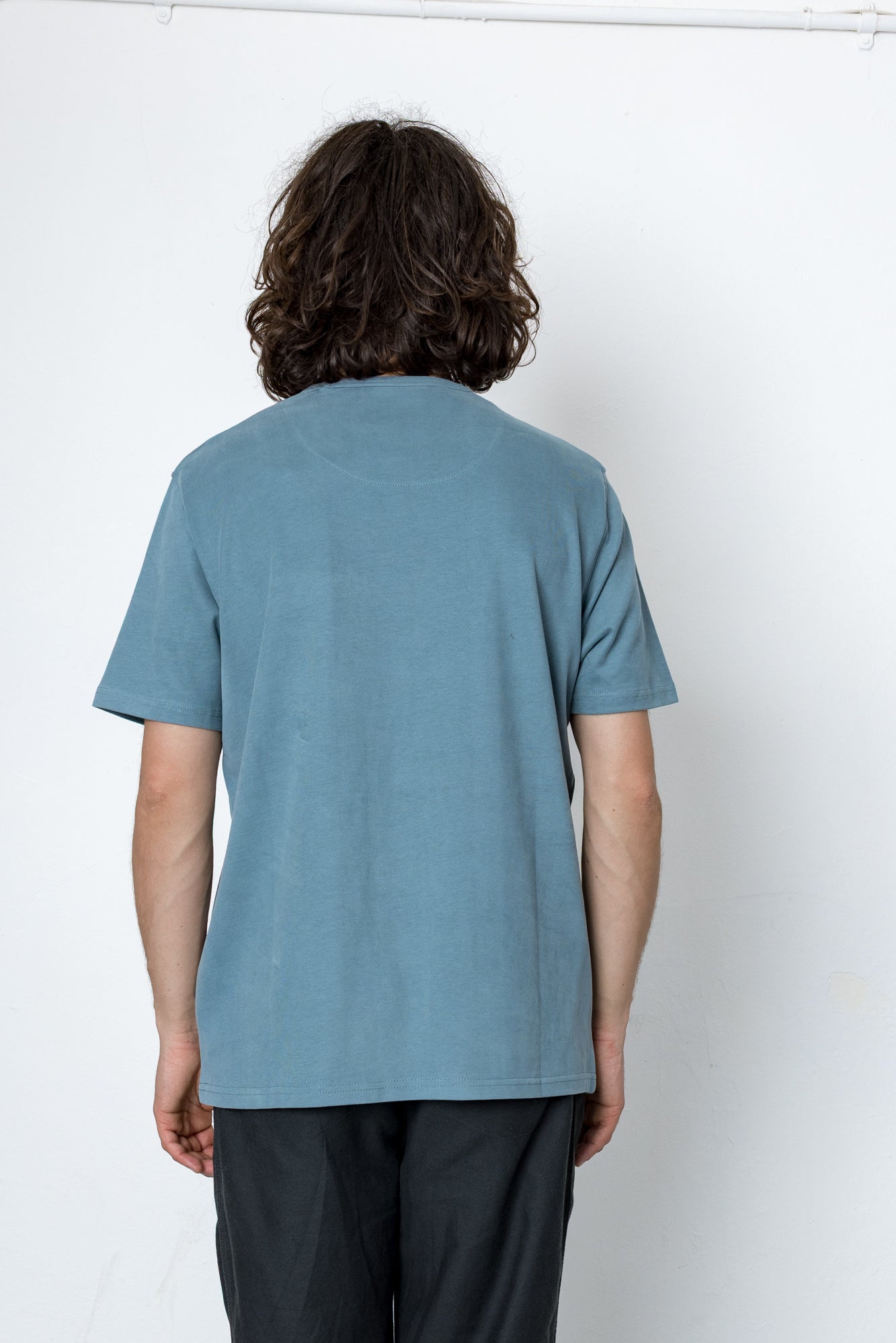 Person wearing light blue t-shirt facing a white wall
