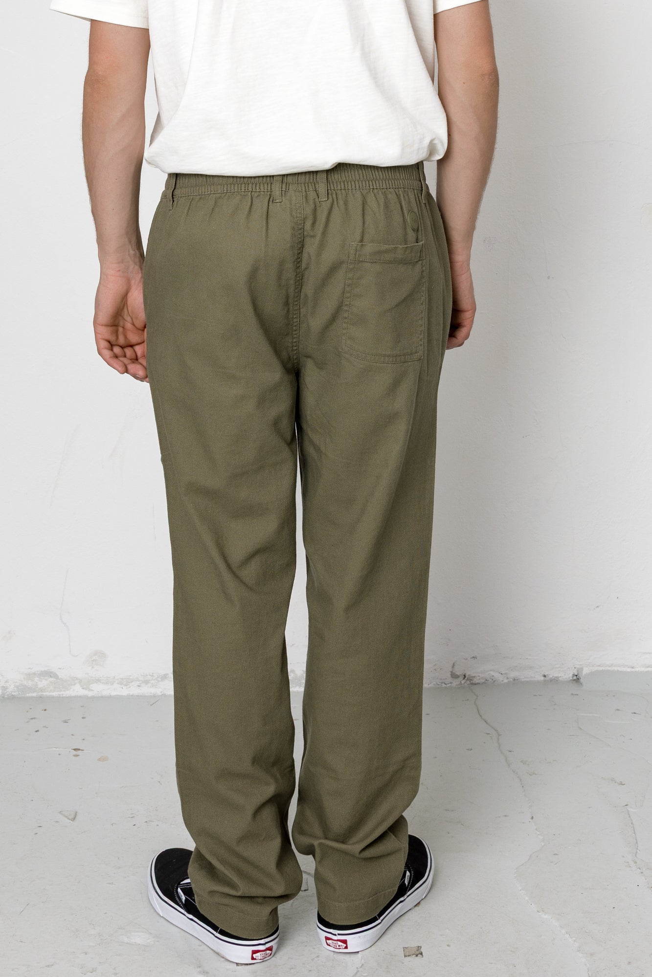 Person wearing olive green pants and a white shirt against a plain background