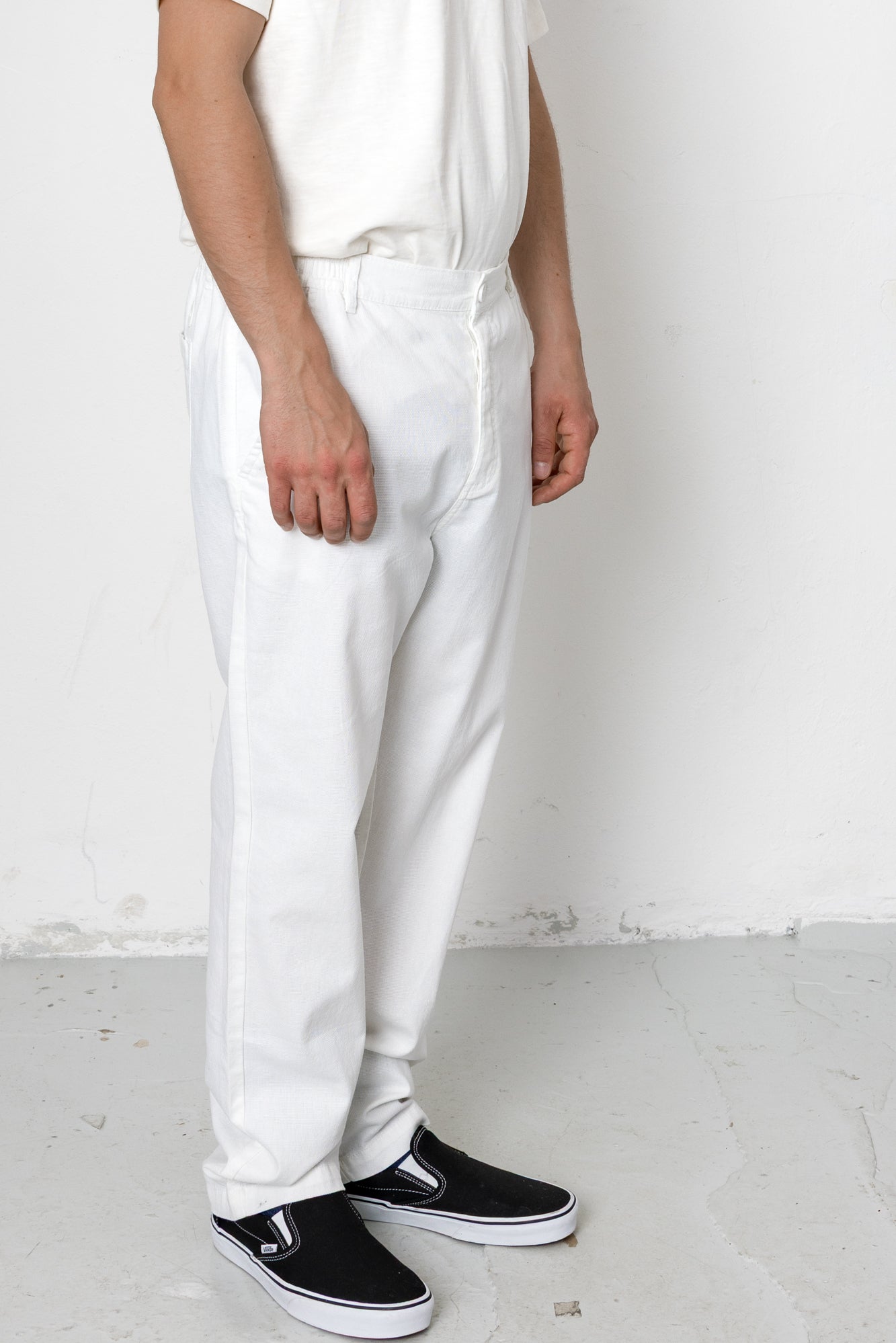 Person wearing white pants and black shoes against a plain background