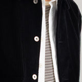 Close-up of a person wearing a black corduroy jacket over a white collared shirt with black horizontal stripes.