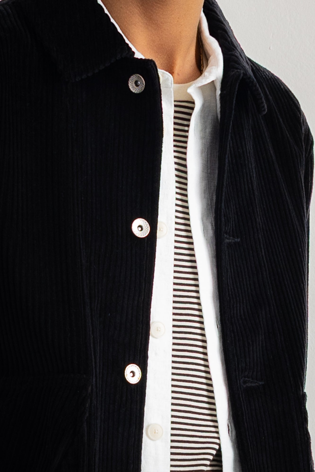 Close-up of a person wearing a black corduroy jacket over a white collared shirt with black horizontal stripes.