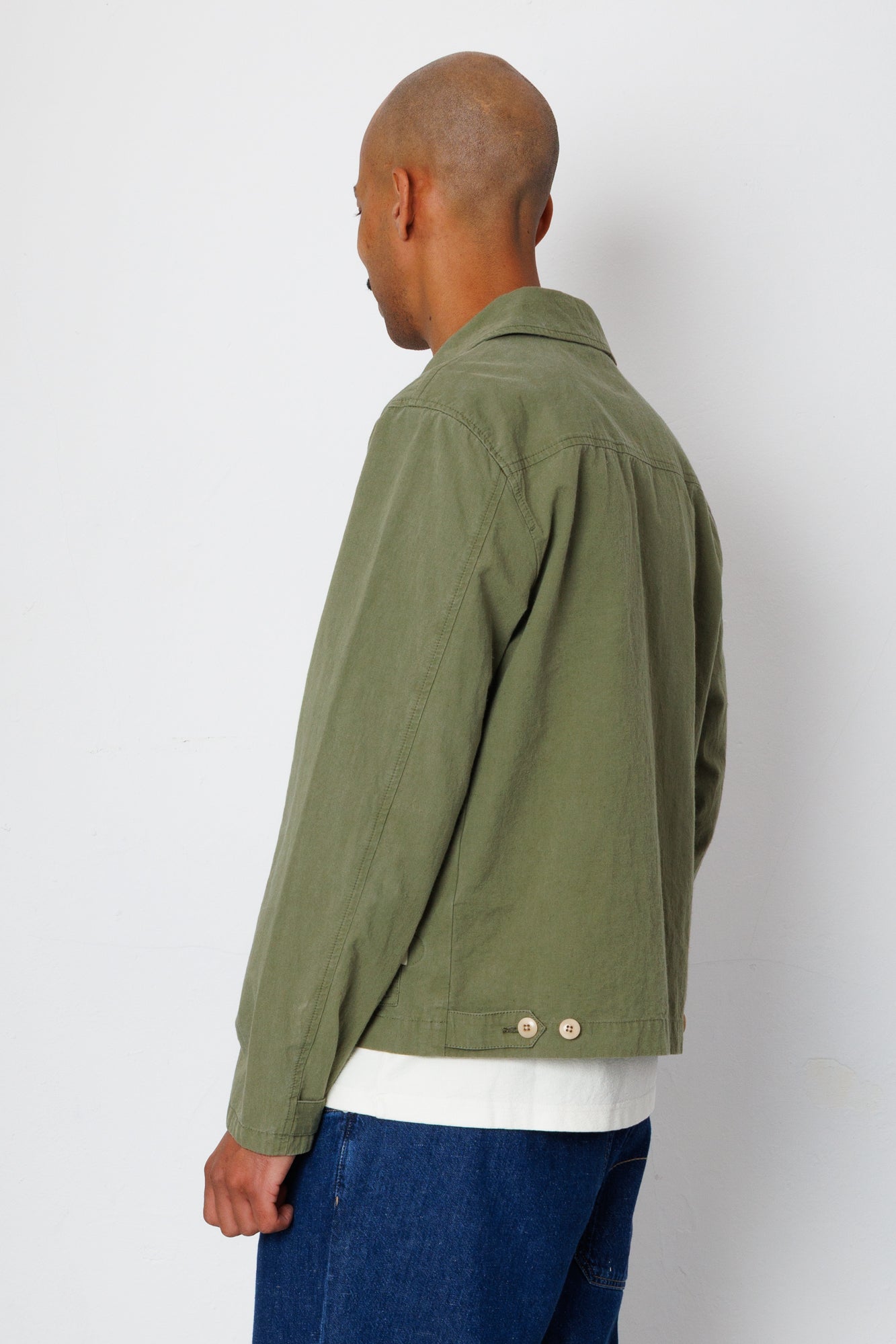 Person wearing a green jacket and blue jeans against a white background
