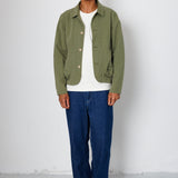Man wearing a green jacket, white shirt, blue pants, and black sneakers against a white background
