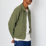 Man wearing a green jacket over a white shirt and blue jeans on a plain background
