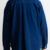 A person shown from the back wearing a dark indigo blue long-sleeve shirt and green pants against a plain white background.