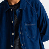A close-up of a person wearing a dark indigo blue denim button-up shirt over a black and white striped t-shirt, against a plain white background.
