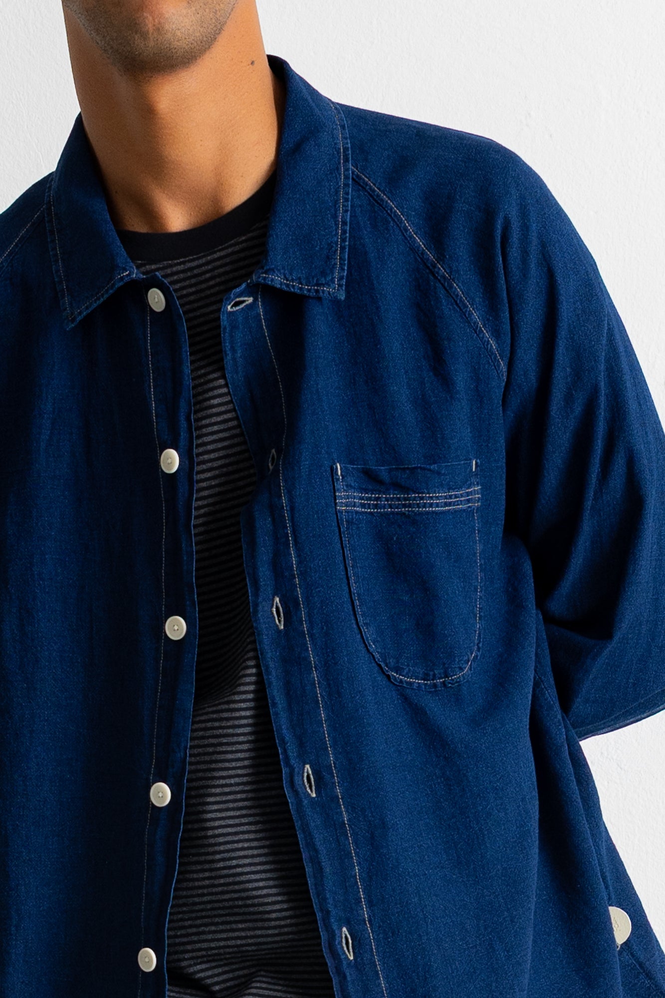 A close-up of a person wearing a dark indigo blue denim button-up shirt over a black and white striped t-shirt, against a plain white background.
