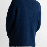 A person shown from the back wearing a dark navy ribbed knit sweater over a white striped shirt, against a plain white wall.