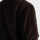 Close-up of a person wearing a dark brown corduroy jacket, showing the ribbed texture and collar against a plain light background.