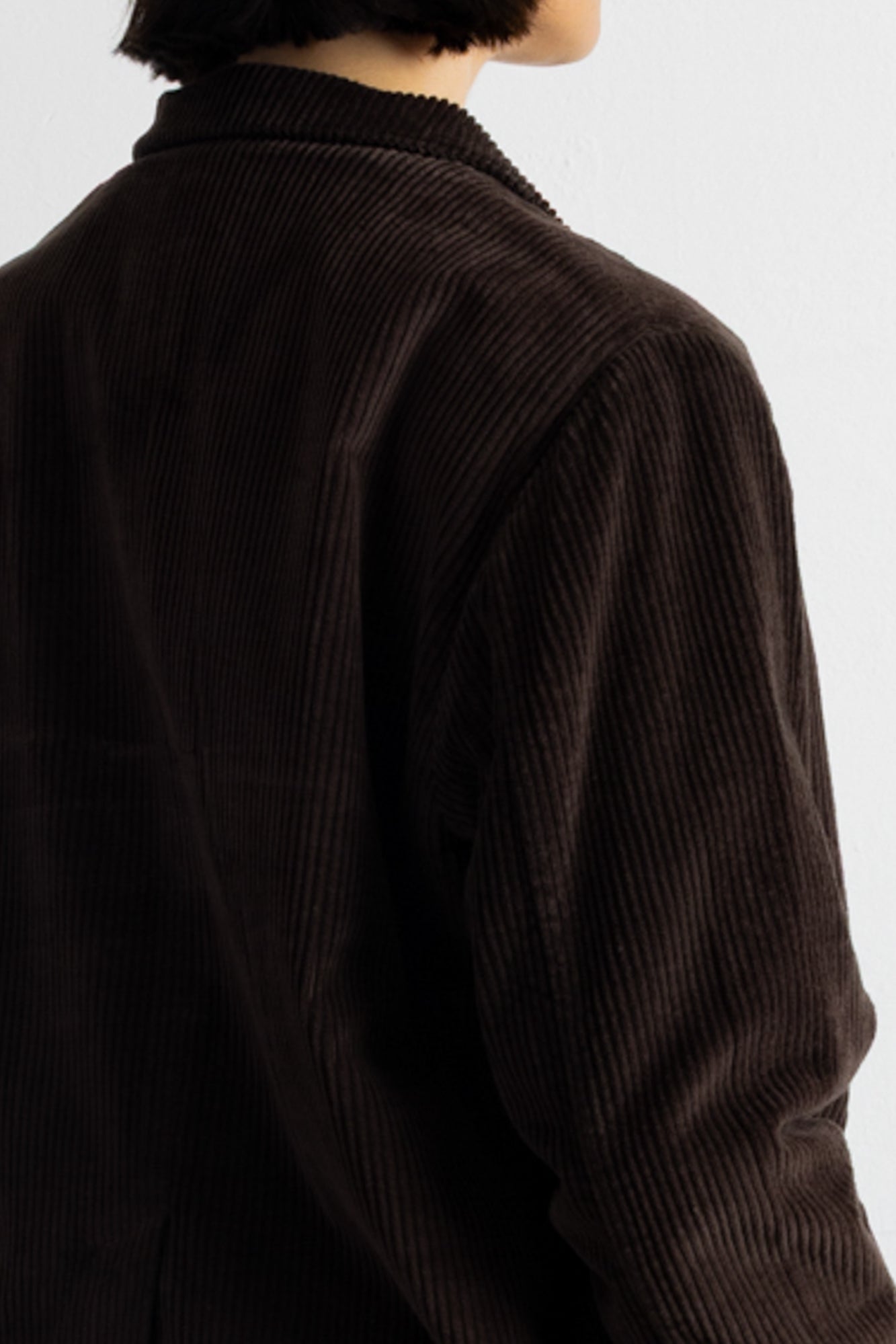 Close-up of a person wearing a dark brown corduroy jacket, showing the ribbed texture and collar against a plain light background.