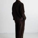 A model shown from the back wearing a dark brown corduroy jacket and matching wide-leg trousers, standing against a plain white studio background.